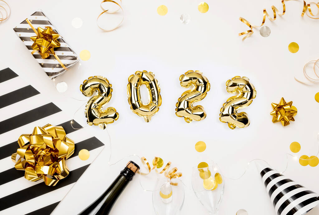 Mutlu yıllar 2022 kutlama kartı. Beyaz arka planda 2022 sayılı altın folyo balonları. Hediyeler ve parti şapkaları. - Fotoğraf, Görsel