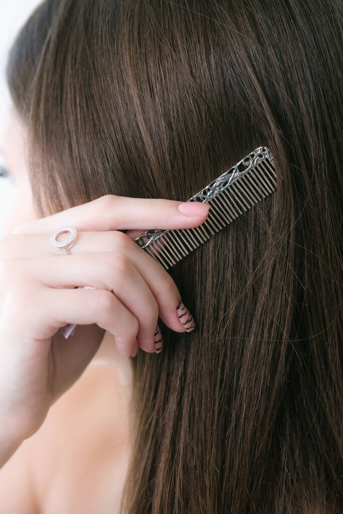 Uzun siyah saçlı çekici bir genç kız saçını taramak için gümüş bir tarak kullanır. Güzellik ve moda  - Fotoğraf, Görsel