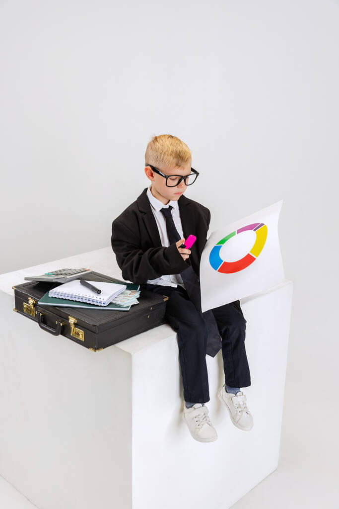 Portret małego chłopca, dziecięcy biznesmen w ogromnym garniturze ojca z dużym retro walizki attache izolowane na białym tle studio. - Zdjęcie, obraz