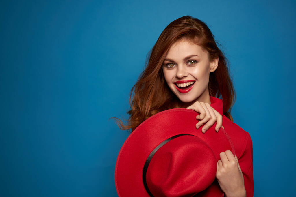 όμορφη γυναίκα φορώντας ένα κόκκινο καπέλο καλλυντικά που θέτουν μπλε φόντο - Φωτογραφία, εικόνα