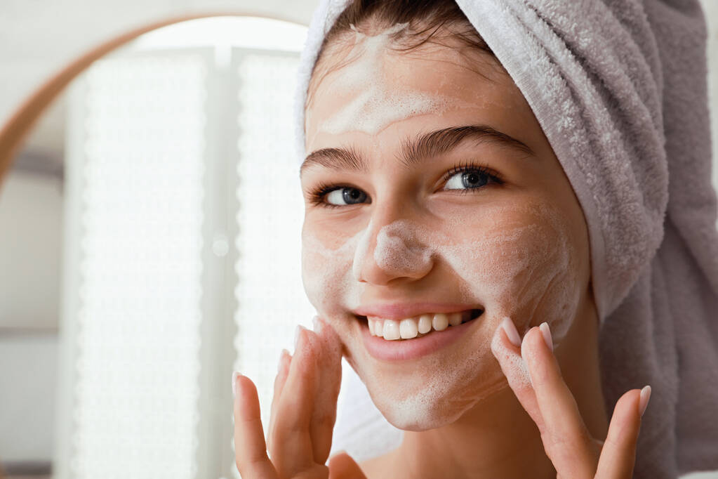 Menina adolescente bonita aplicando espuma de limpeza no rosto no banheiro, close-up. Cuidado da pele cosmético - Foto, Imagem