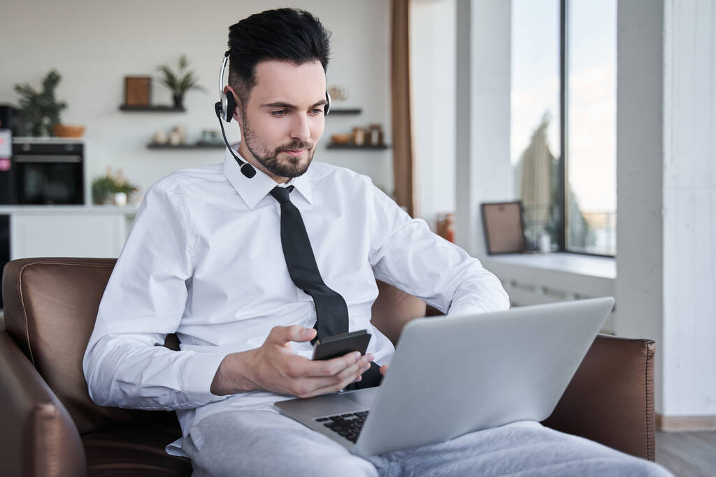 Man wearing headset sitting at the armchair and looking attentively at the laptop screen - Photo, Image