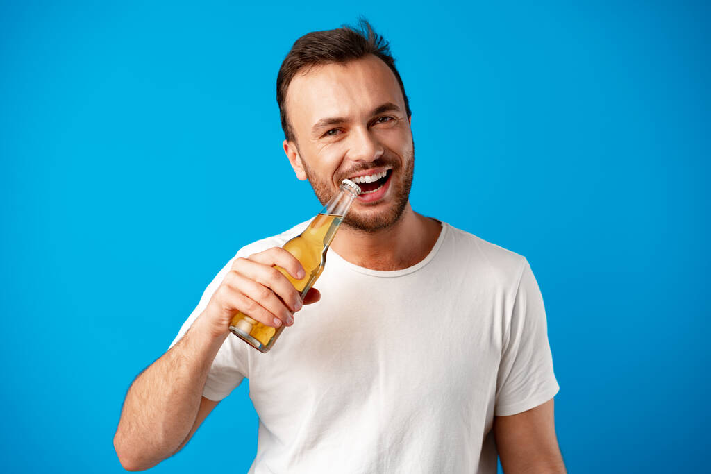 Allegro giovane uomo in t-shirt con bottiglia di birra sullo sfondo blu - Foto, immagini