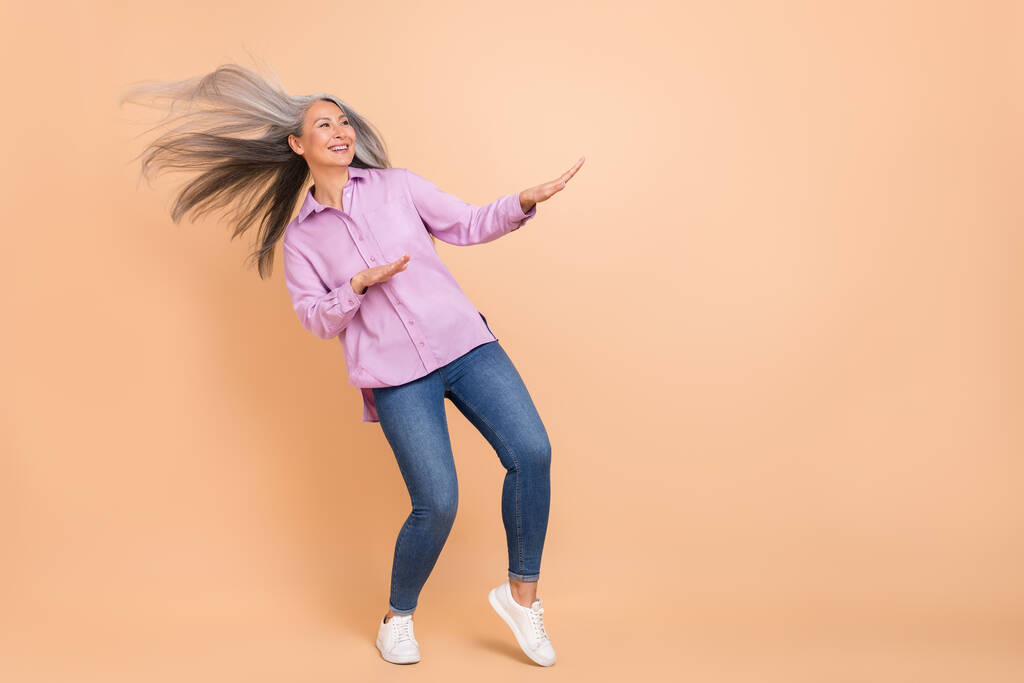 Фотографія повного розміру прохолодного білого зачіски літньої леді танцюють рекламний одяг фіолетовий одяг джинси кросівки ізольовані на бежевому фоні
 - Фото, зображення