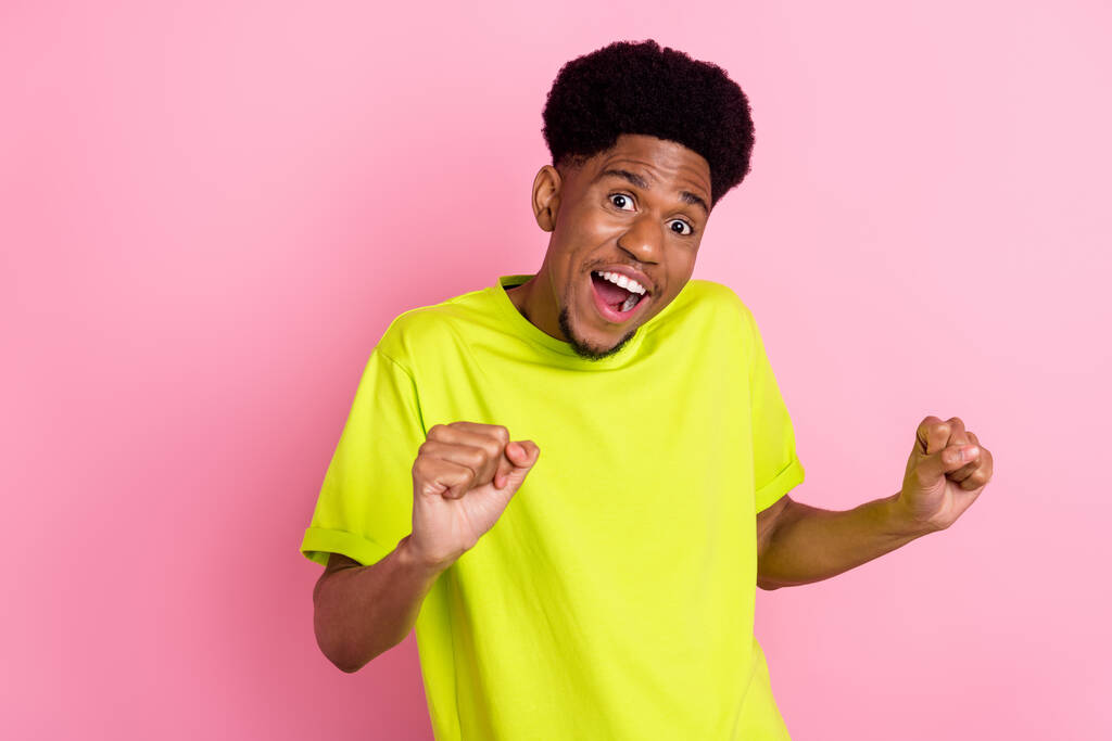Foto van vrolijke afro-Amerikaanse jongeman goede humeur winnaar dragen limoen t-shirt geïsoleerd op pastel roze kleur achtergrond - Foto, afbeelding