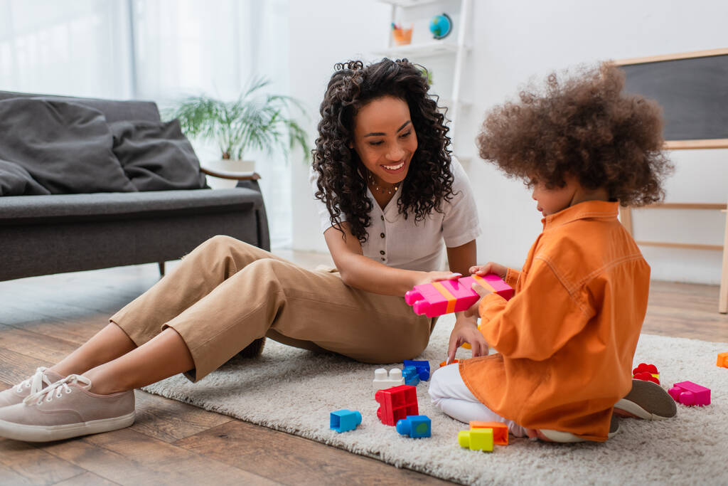 Positivo afro-americano madre seduta vicino figlia giocare mattoni a casa  - Foto, immagini