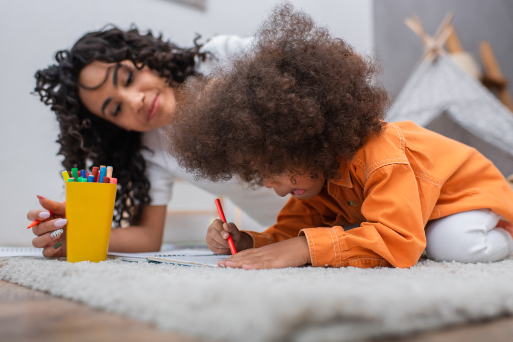 africano americano niño dibujo en notebook cerca borrosa mamá en casa  - Foto, Imagen