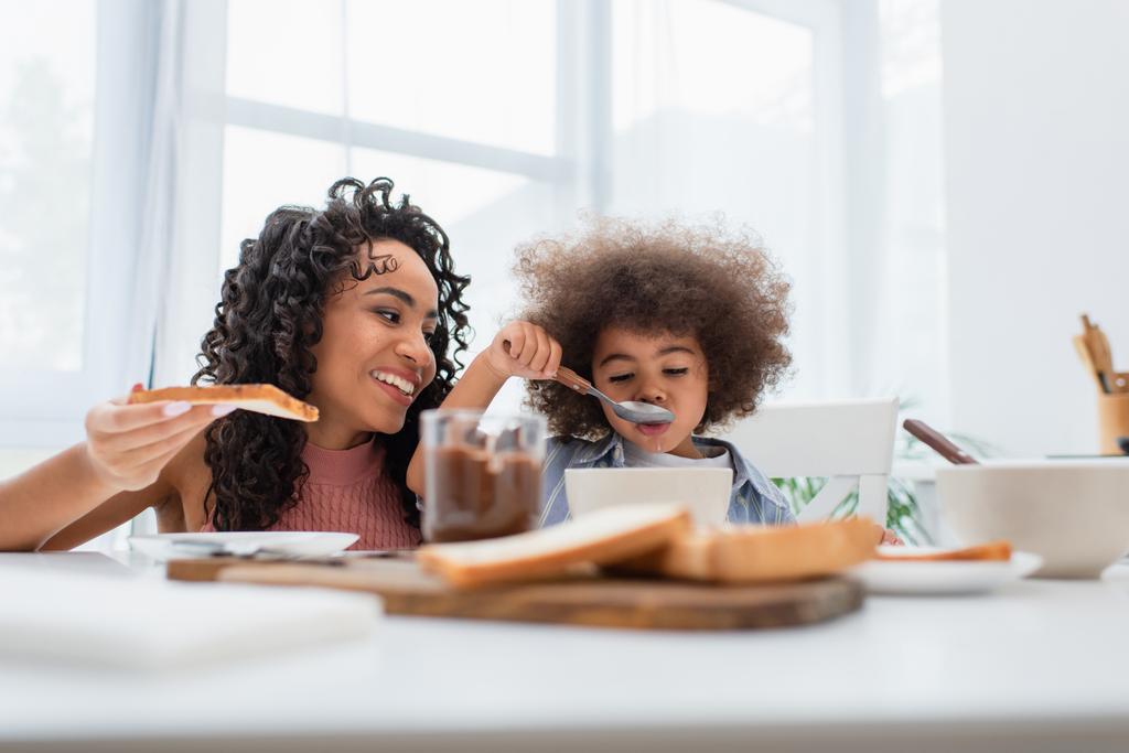 genitore afroamericano che tiene il pane mentre la figlia mangia cereali a casa  - Foto, immagini