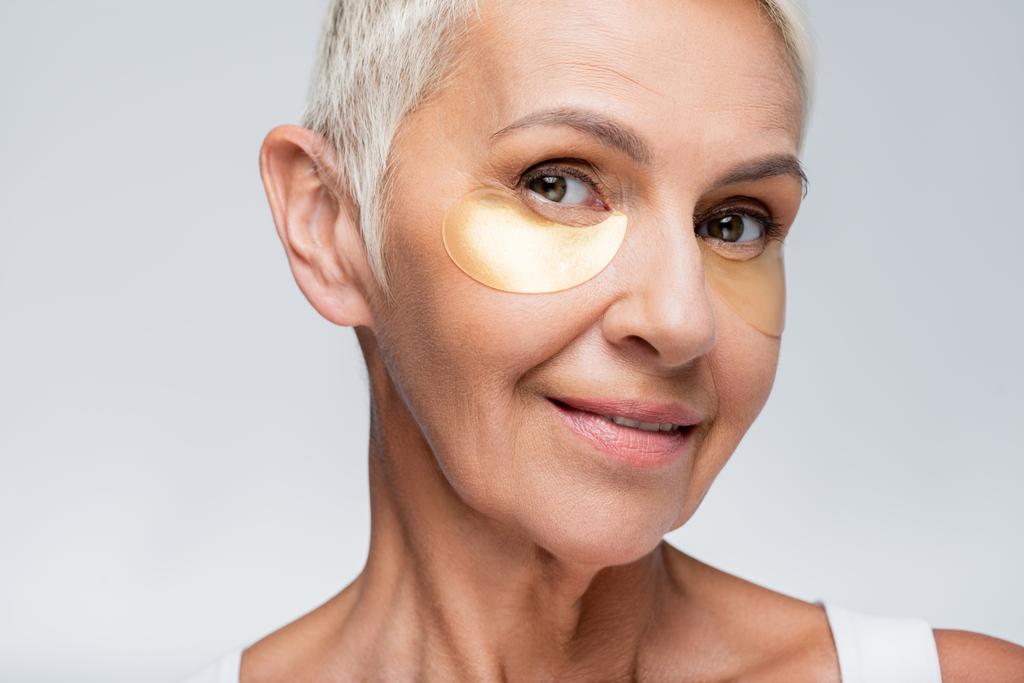 donna anziana sorridente con macchie oculari di collagene isolate sul grigio  - Foto, immagini