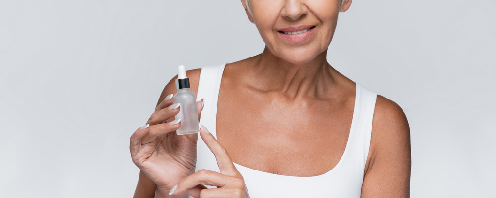 cropped view of happy senior woman holding bottle with serum isolated on grey, banner - Photo, Image