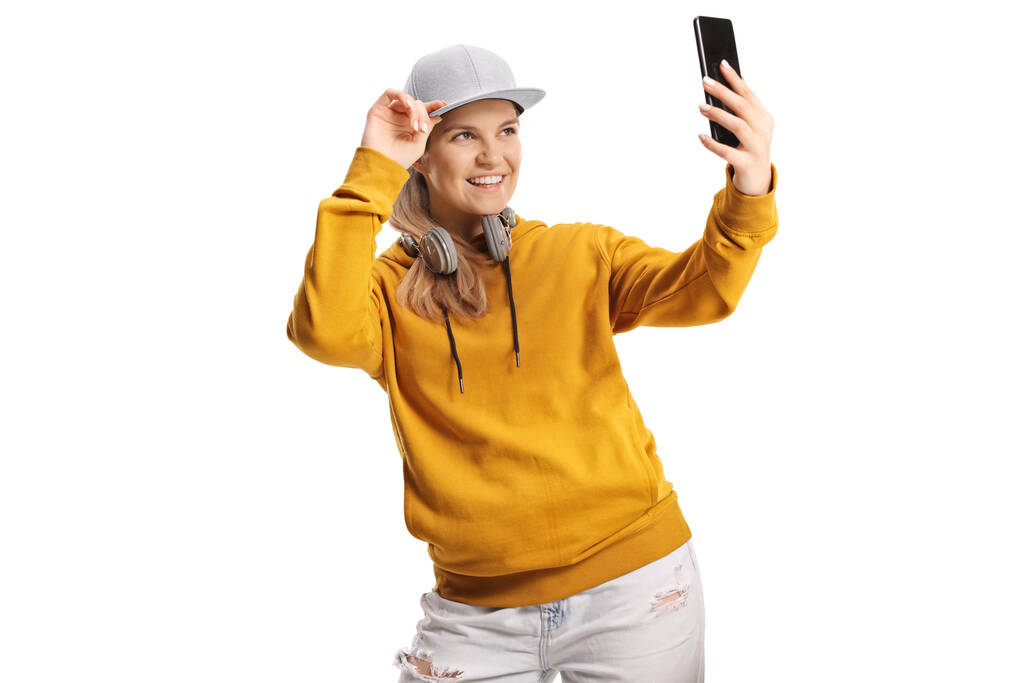 ヘッドフォンを持つ若い女性は白い背景に隔離されたスマートフォンで自撮り - 写真・画像