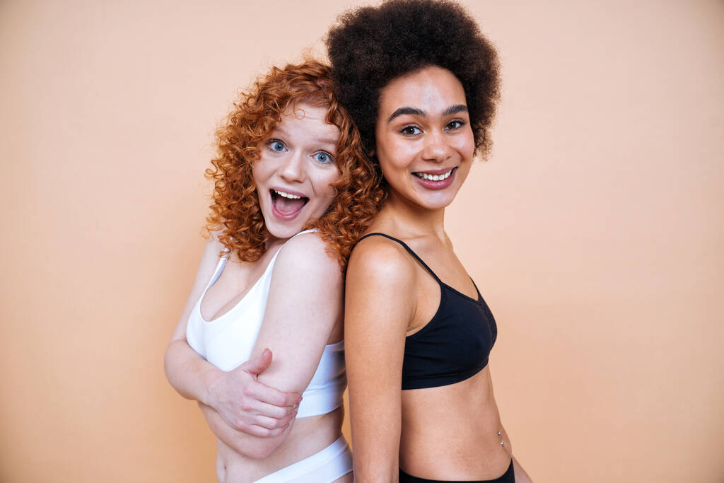 Stüdyoda pozitiflik için poz veren farklı ten ve vücuda sahip iki genç kadının güzel görüntüsü. Renkli arka planlarda iç çamaşırlı kadın modeller. - Fotoğraf, Görsel