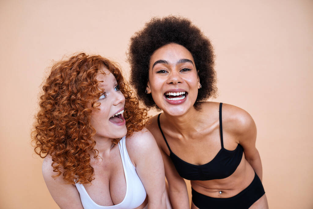 szépség kép két fiatal nő különböző bőr és test pózol stúdióban a test pozitív fotózás. Vegyes női modellek fehérnemű színes hátterű - Fotó, kép