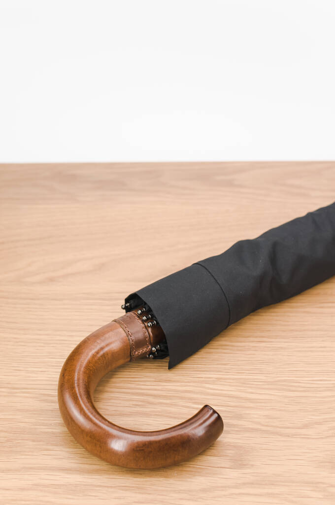 paraguas plegable negro con mango de madera maciza sobre una superficie de madera con espacio para copiar - Foto, Imagen