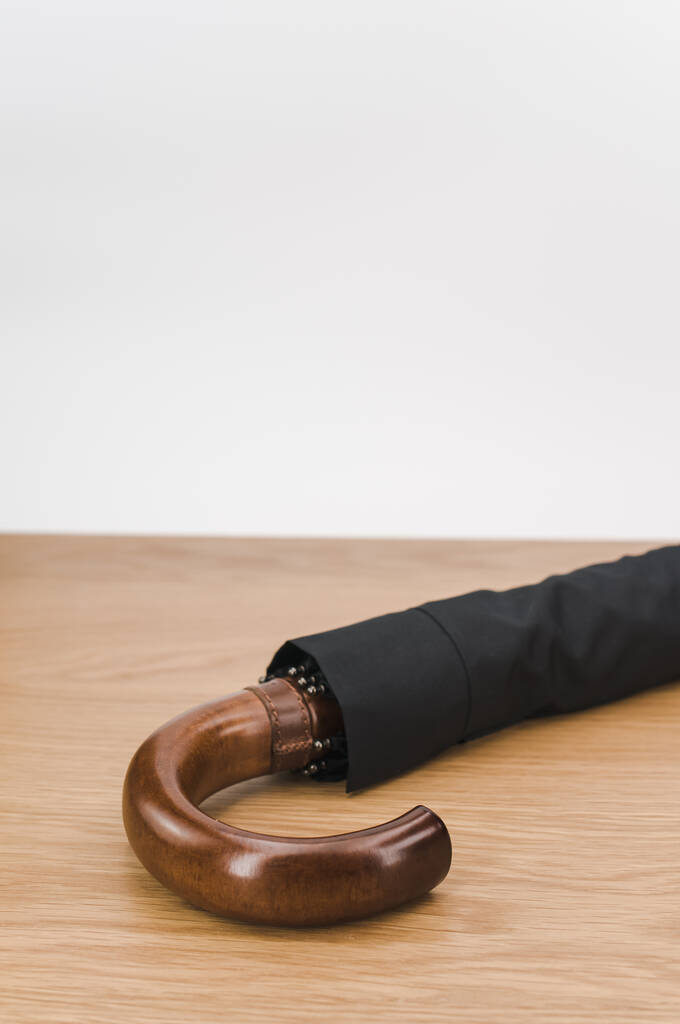 black foldable umbrella with solid wood handle on a wooden surface with copy space - Foto, Imagem