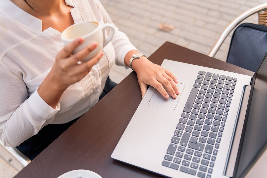 Unerkennbare Geschäftsfrau, die mit ihrem Laptop arbeitet, während sie Kaffee auf einer Terrasse trinkt, Konzept der digitalen Unternehmerin und urbaner Lebensstil - Foto, Bild