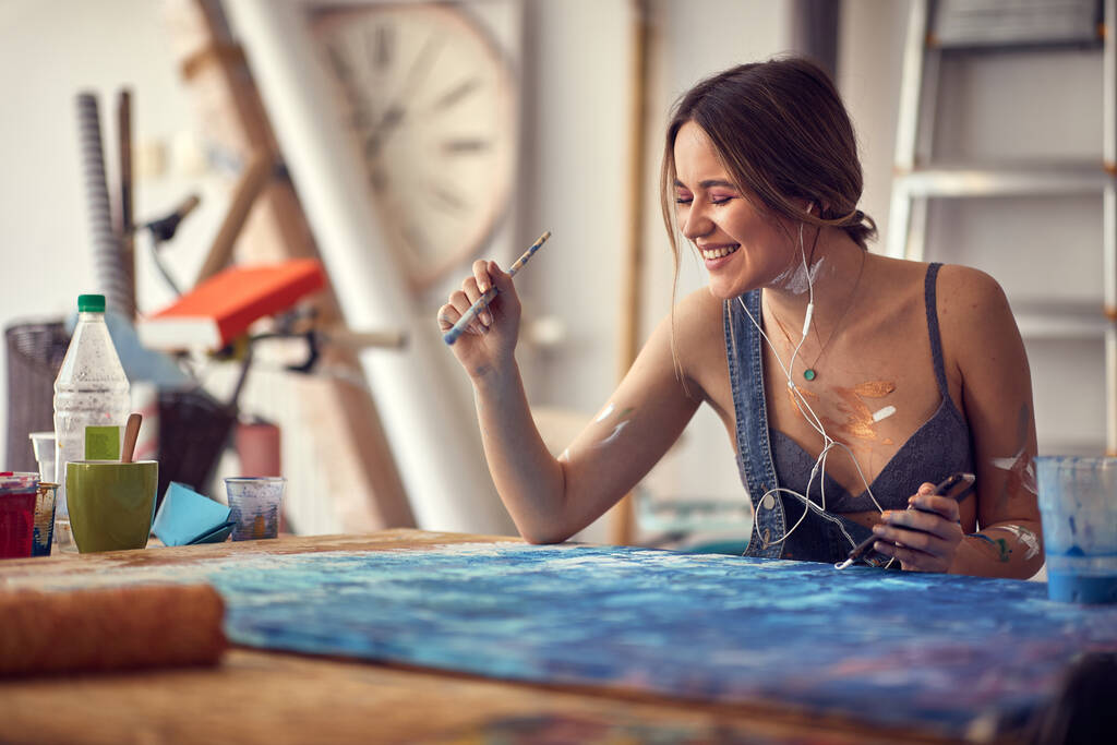 A young sexy and attractive female artist loves to paint in a pleasant atmosphere in her studio while listening to the music. Art, painting, studio - Photo, Image