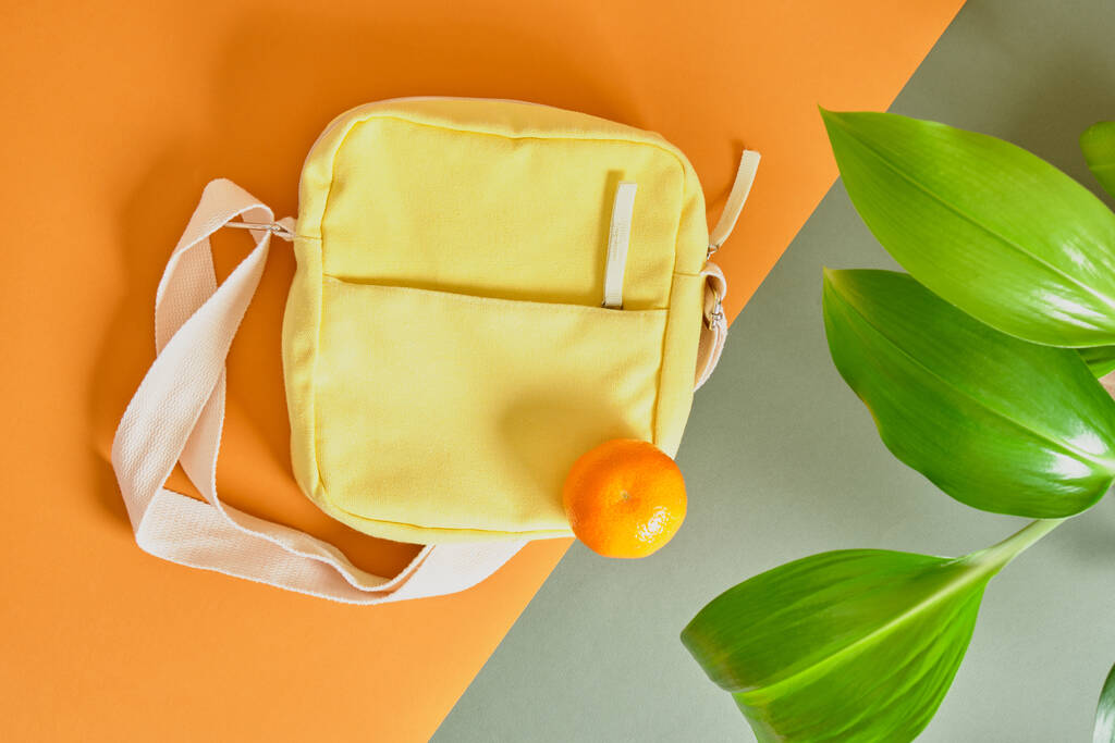 σάκος από άχρηστα φρούτα, ύφασμα από φύλλα και άχρηστα τρόφιμα, κίτρινη υφασμάτινη σακούλα και φλούδα πορτοκαλιού σε πράσινο φόντο - Φωτογραφία, εικόνα