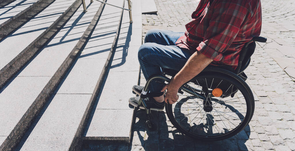 Молодой человек с ограниченными физическими возможностями в инвалидной коляске перед лестницей - Фото, изображение