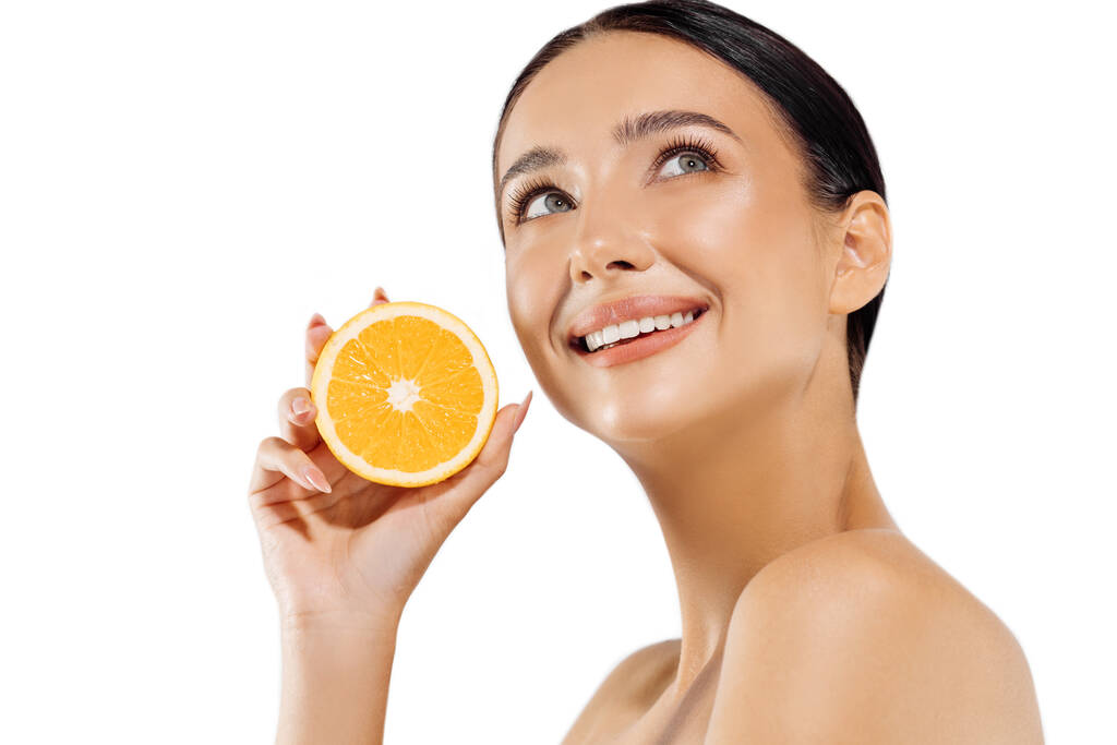 Ritratto donna e frutta. Un modello felice tiene un arancio succoso vicino al viso e guarda la fotocamera su uno sfondo bianco. Bella ragazza utilizza agrumi e vitamine naturali per una pelle sana - Foto, immagini