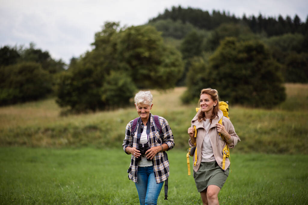 Femme âgée active avec jumelles randonnée avec sa fille adulte à l'extérieur dans la nature. - Photo, image