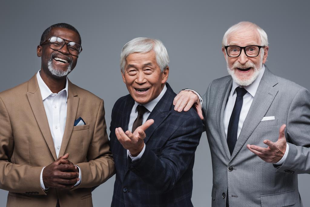 старші багатоетнічні бізнесмени з простягнутими руками біля усміхненого афроамериканського колеги ізольовані на сірому
 - Фото, зображення