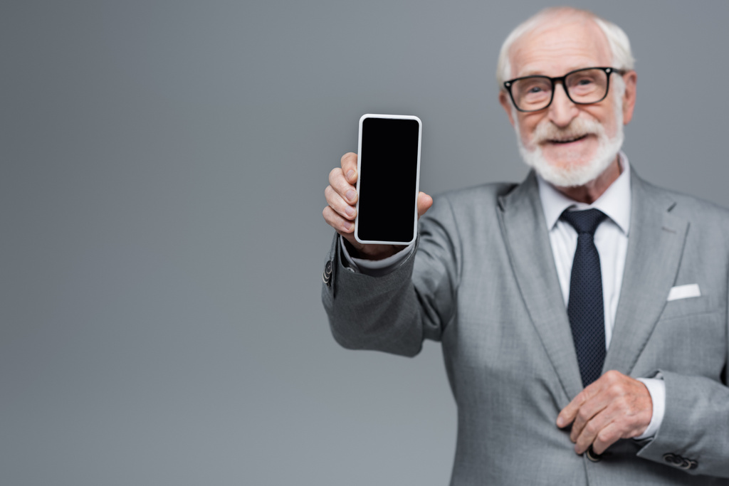 θολή ανώτερος επιχειρηματίας δείχνει κινητό τηλέφωνο με λευκή οθόνη απομονώνονται σε γκρι - Φωτογραφία, εικόνα