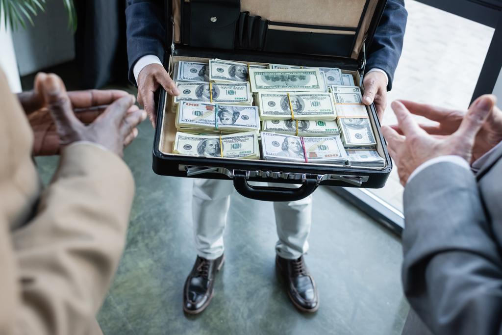 részleges kilátás elmosódott üzleti partnerek közelében ember dollár aktatáskában - Fotó, kép