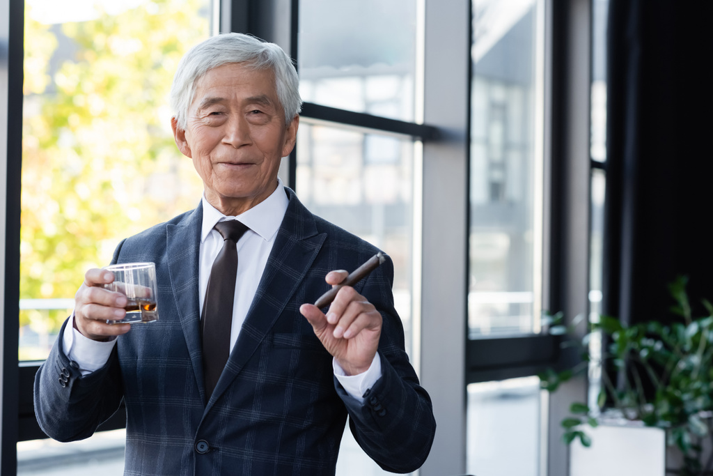 senior asiatique homme d'affaires avec cigare et verre de whisky souriant à la caméra dans le bureau - Photo, image