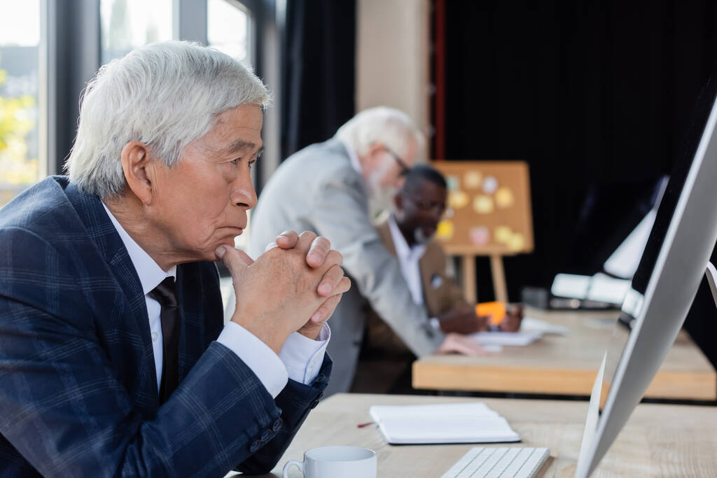 senior asian businessman looking at computer monitor near blurred multiethnic colleagues - Photo, Image