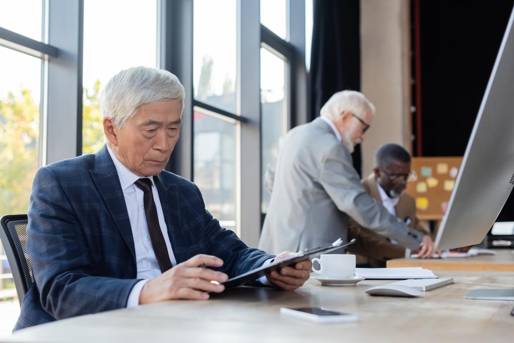 senior aziatische zakenman werken met document in de buurt wazig interraciale collega 's - Foto, afbeelding