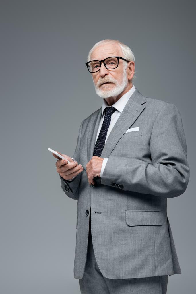 старший уверенный в себе бизнесмен с мобильным телефоном глядя на камеру, изолированную на серый - Фото, изображение