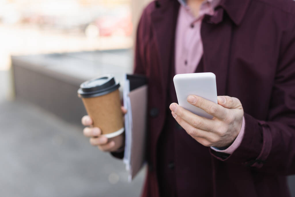 Vágott kilátás elmosódott üzletember papír pohár és mappák gazdaság okostelefon szabadban  - Fotó, kép