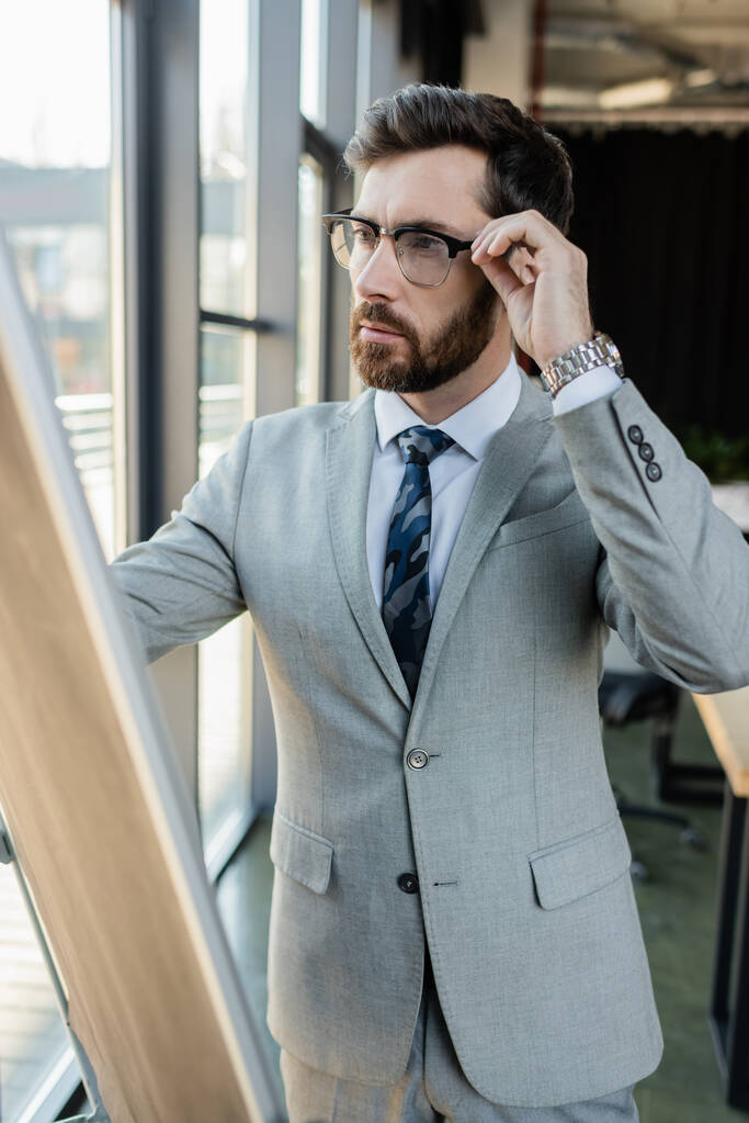 Uomo d'affari in occhiali in piedi vicino a flip chart in ufficio  - Foto, immagini
