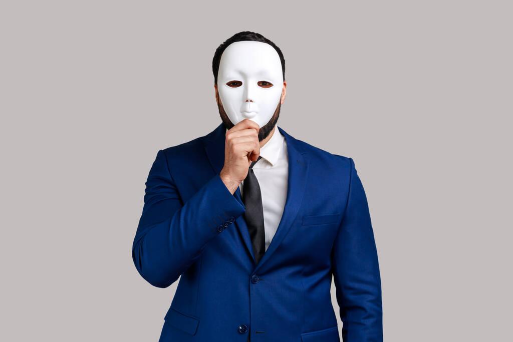 Anonymer unbekannter Geschäftsmann, der ihr Gesicht mit einer weißen Maske verhüllt und ihre wahre Persönlichkeit verbirgt, Anonymität, er trägt Anzug im offiziellen Stil. Indoor Studio isoliert auf grauem Hintergrund gedreht. - Foto, Bild