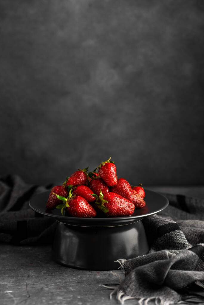 A vertical shot of fresh strawberries on a black plate with a monochrome background - Photo, Image