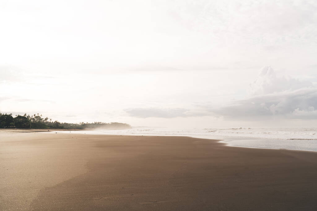 Живописный пейзаж пенных волн бесконечного океана, прокатившихся по удивительному пустому мокрому песчаному пляжу против облачного неба в экзотической стране - Фото, изображение