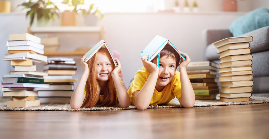 Два милых ребенка лежат на полу в помещении с книгами на голове. - Фото, изображение