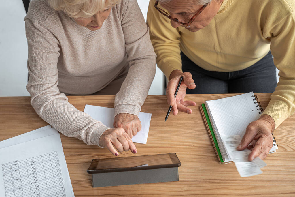 Сосредоточенные старший муж и жена сидят за столом дома и смотрят на экран планшета - Фото, изображение
