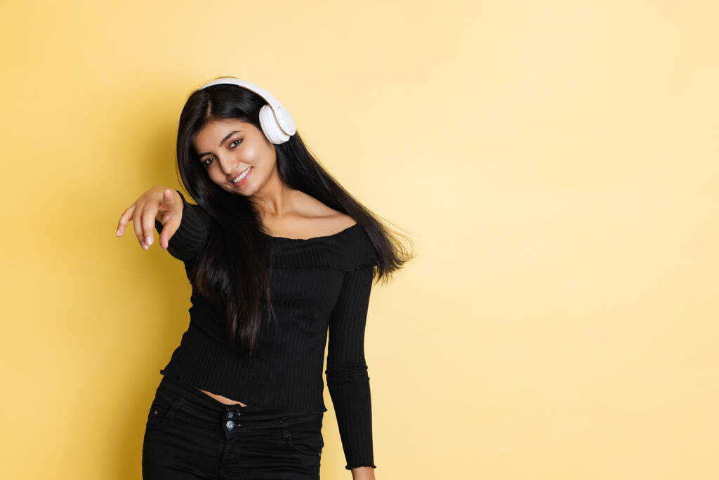 Emocionální mladý rozkošný roztomilý dívka, student v černé blůze poslech hudby ve sluchátkách izolovaných na žluté barvy studio pozadí - Fotografie, Obrázek