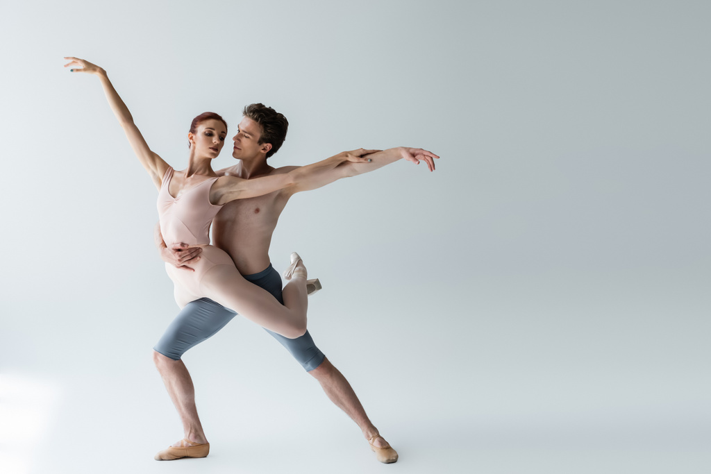 повнометражний без сорочки чоловік і молода жінка в боді-костюмі виконують балетний танець на сірому
 - Фото, зображення
