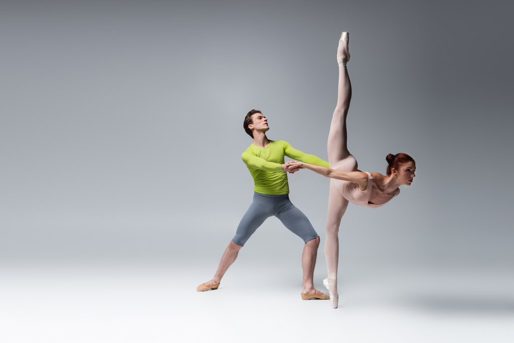 полная длина артиста балета, поддерживающего балерину во время танца на темно-сером - Фото, изображение