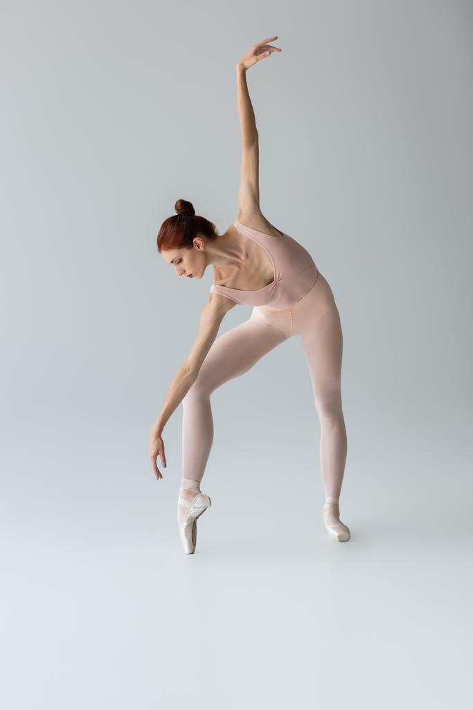 larga duración de bailarina en zapatillas de ballet bailando con la mano extendida sobre gris - Foto, imagen