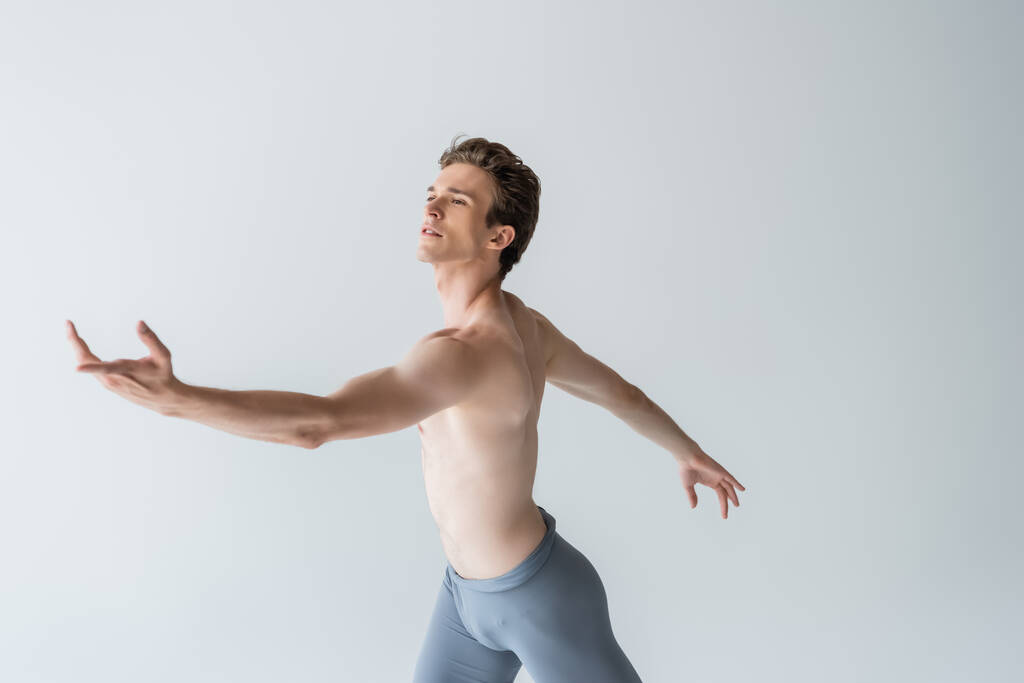 joven bailarina de ballet sin camisa realizando danza aislada sobre gris  - Foto, Imagen