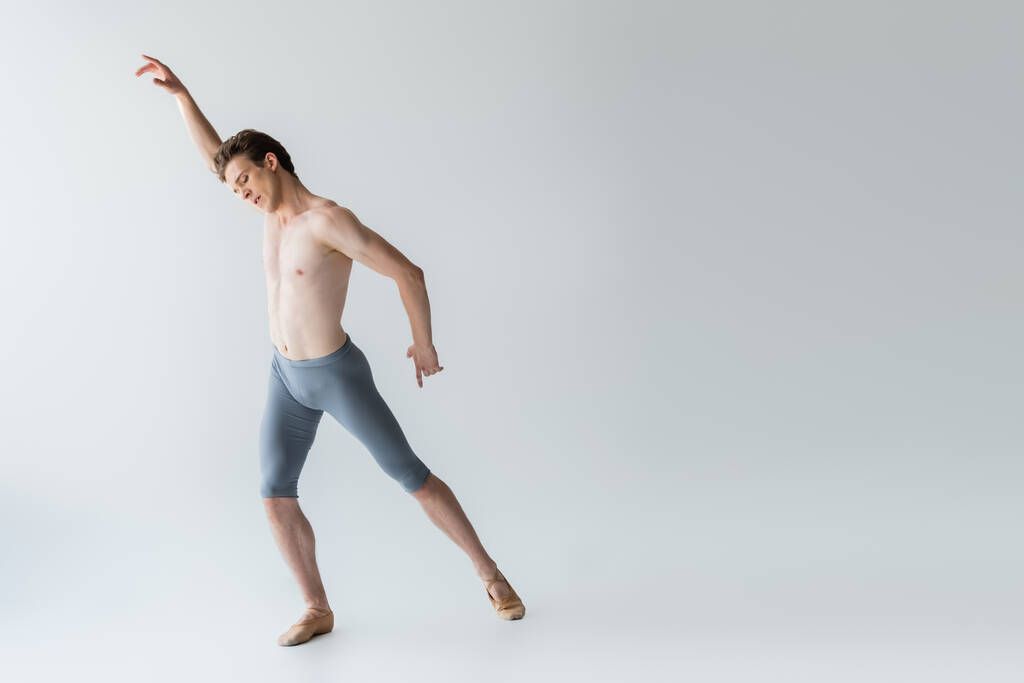 longitud completa de la joven bailarina de ballet sin camisa realizando danza de ballet en gris  - Foto, imagen