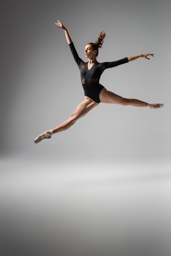 Bailarina ligera en zapatos puntiagudos y body negro saltando sobre gris oscuro - Foto, Imagen