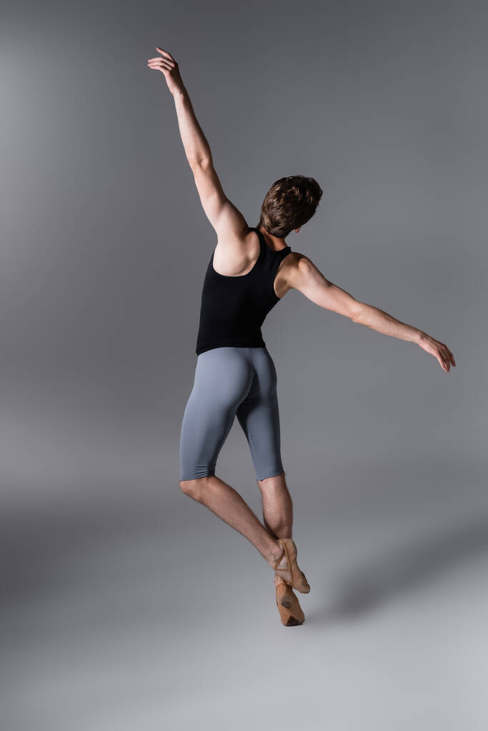 vista posteriore del giovane in scarpette da balletto che esegue danza classica su grigio scuro - Foto, immagini