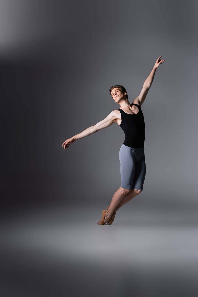 elegante bailarina con las manos extendidas realizando danza de ballet en gris oscuro  - Foto, Imagen