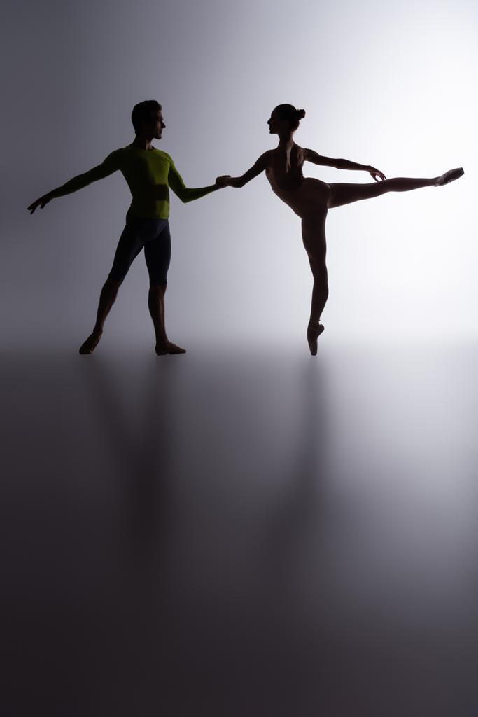 side view of graceful ballerina in bodysuit dancing with partner on dark grey - Photo, Image
