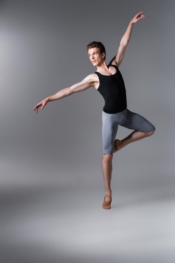 junge Tänzerin im Tank-Top gestikuliert beim Balletttanz auf dunkelgrau - Foto, Bild